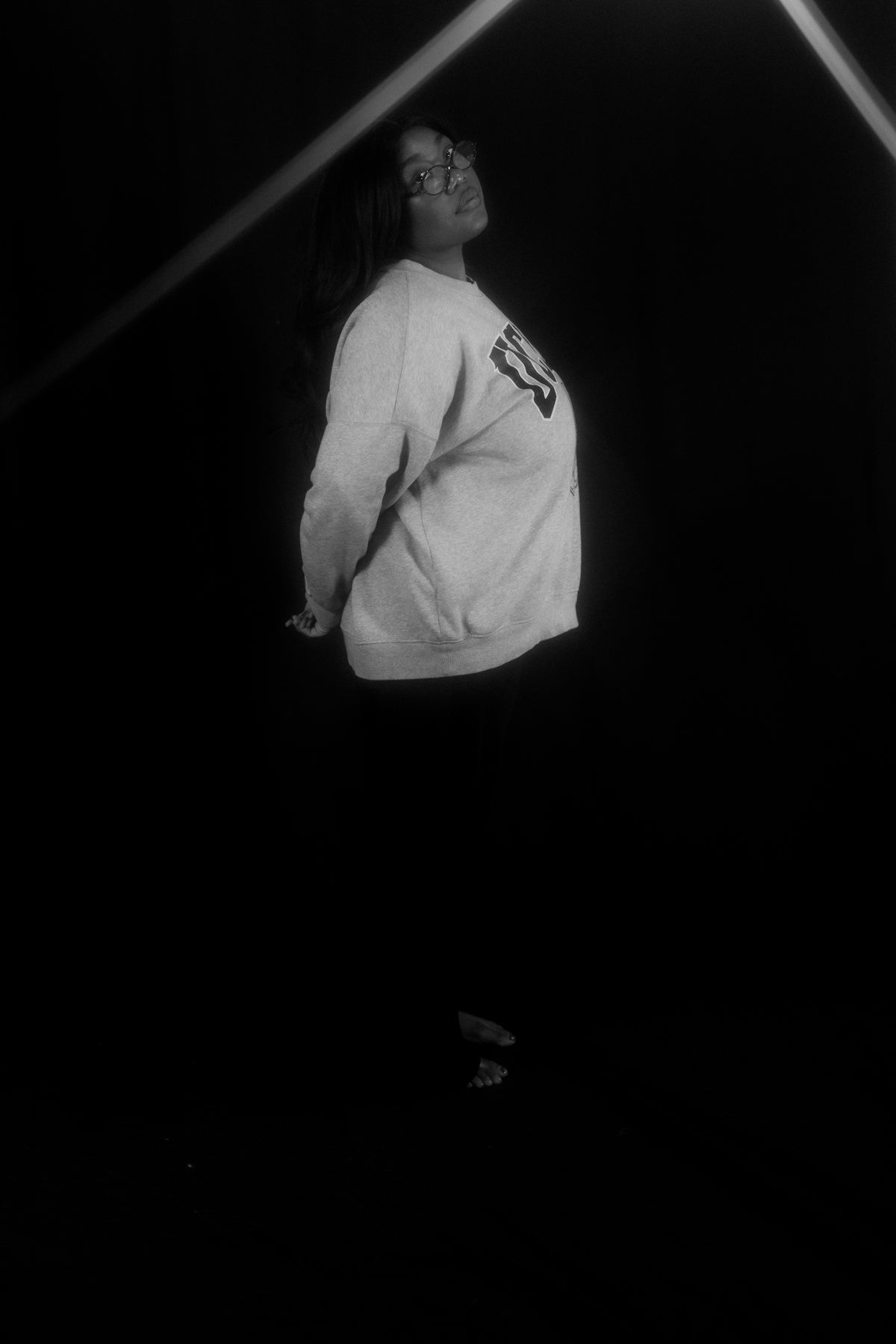 Woman in sweatshirt and dark pants against black background.