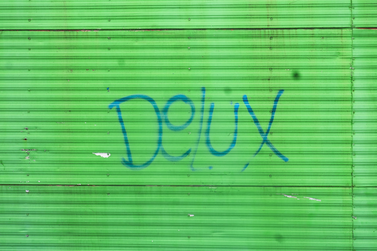 Blue graffiti reading Delux on a bright green corrugated metal wall
